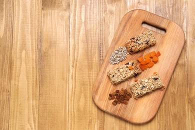 Photo of Different tasty granola bars and ingredients on wooden table, top view. Space for text