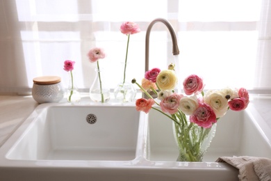 Photo of Beautiful fresh ranunculus flowers in kitchen sink