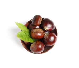 Fresh sweet edible chestnuts with green leaves in wooden bowl on white background, top view