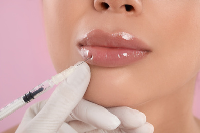 Photo of Young woman getting lips injection on pink background, closeup
