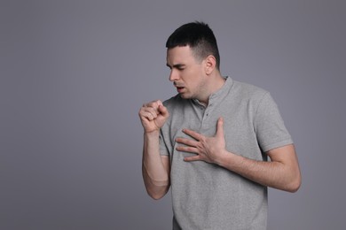 Photo of Young man coughing on grey background, space for text. Cold symptoms