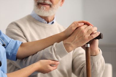 Nurse supporting elderly patient indoors, closeup view