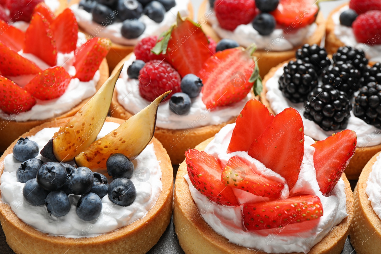 Photo of Many different berry tarts on table, closeup. Delicious pastries