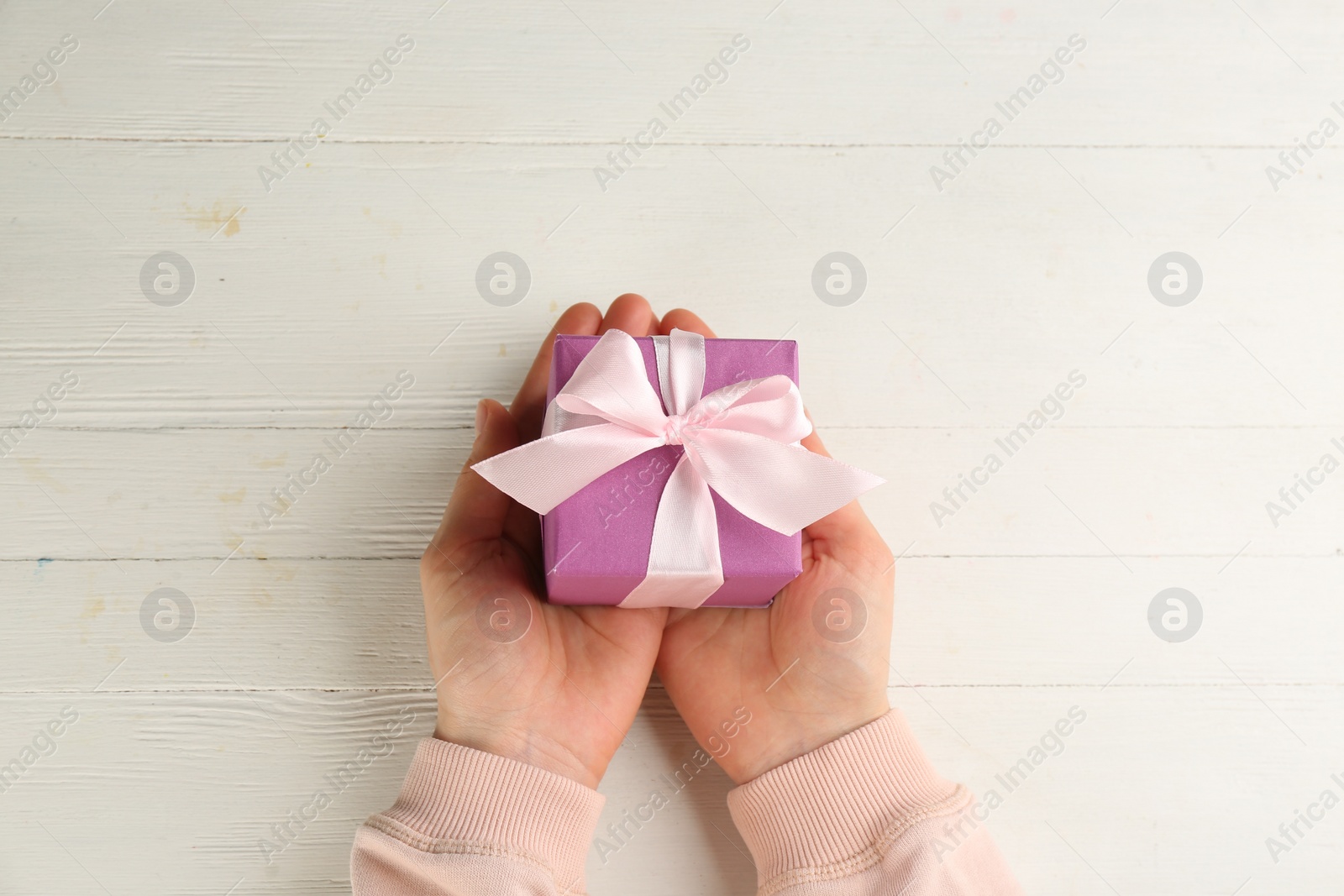 Photo of Woman holding gift box at white wooden table, top view. Valentine's Day celebration