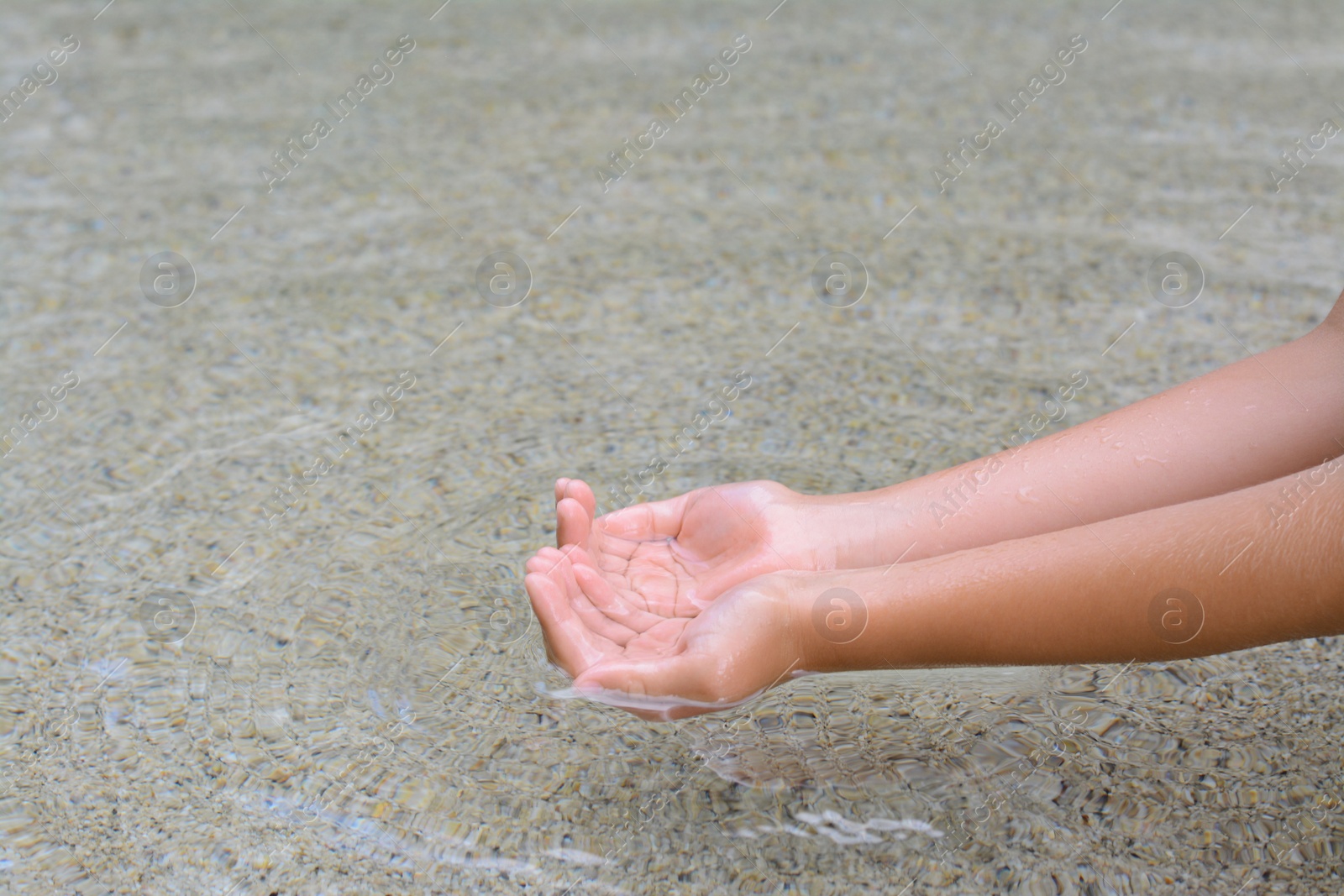 Photo of Kid dipping hands in water outdoors, closeup. Space for text