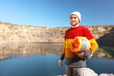 Male camper with sleeping bag near beautiful lake. Space for text