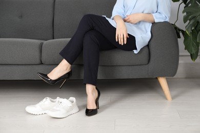 Photo of Comfortable sneakers near businesswoman wearing high heel shoes indoors, closeup