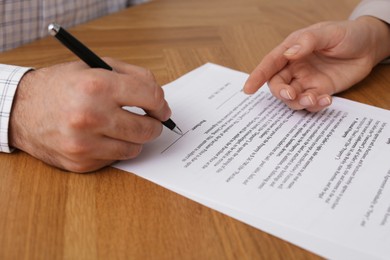 Photo of Businesspeople signing contract at wooden table, closeup of hands