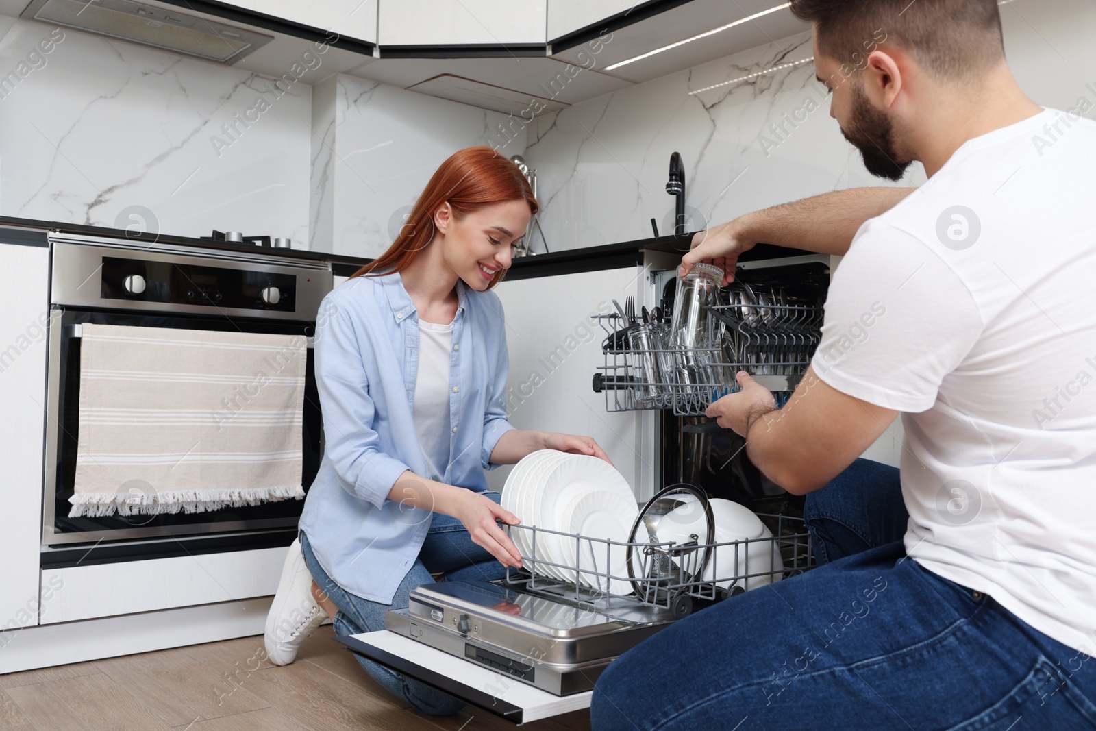 Photo of Lovely couple loading dishwasher with plates in kitchen