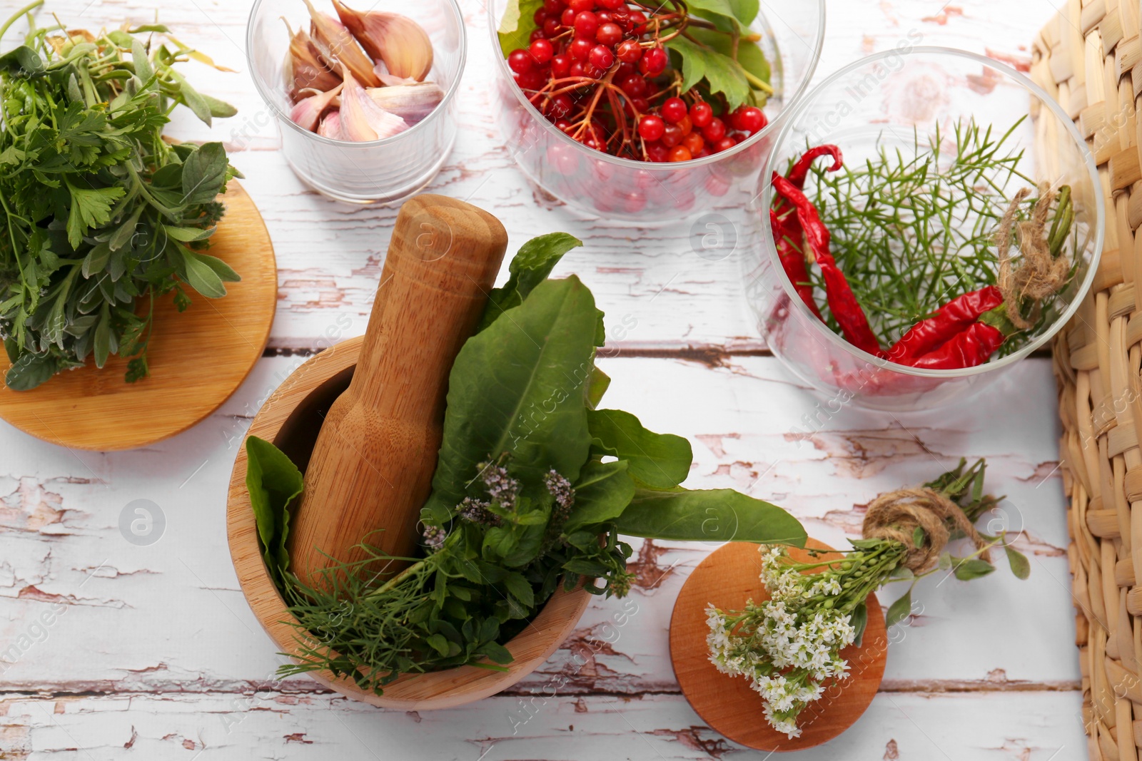 Photo of Mortar with pestle, fresh green herbs and different ingredients on white wooden table, flat lay