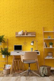 Modern workplace interior with wooden furniture and laptop near yellow brick wall