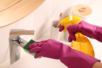 Photo of Woman cleaning faucet with sponge and detergent in bathroom, closeup
