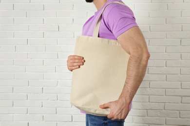 Photo of Man with cotton shopping eco bag against brick wall. Mockup for design