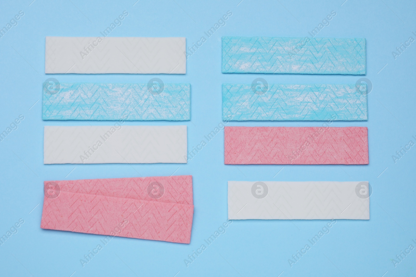 Photo of Sticks of tasty chewing gum on light blue background, flat lay