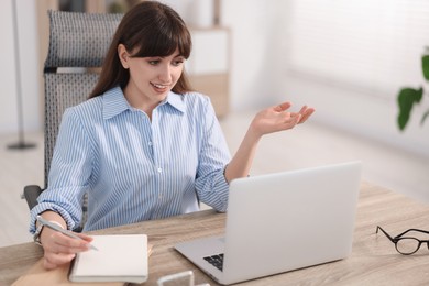 Photo of Woman taking notes during webinar at wooden table indoors