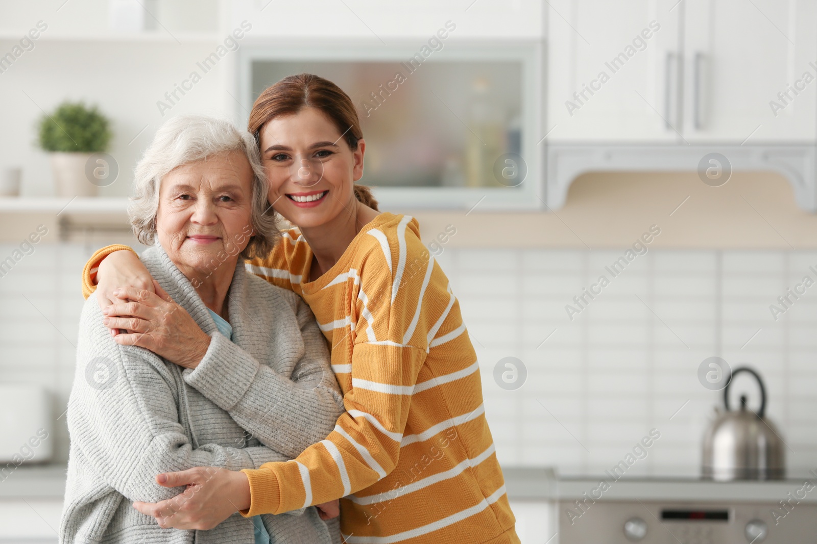 Photo of Elderly woman with female caregiver in kitchen. Space for text