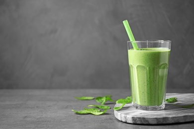 Glass of healthy green smoothie with fresh spinach on grey table, space for text