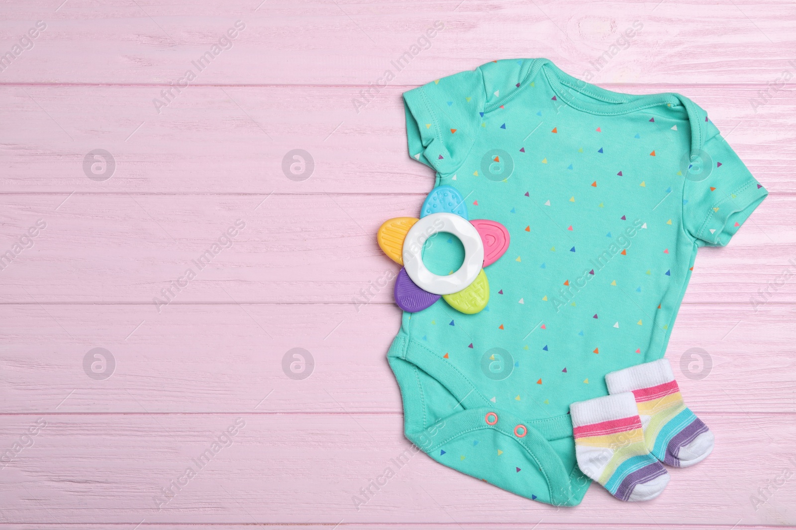 Photo of Child's clothes and teether on pink wooden background, flat lay. Space for text