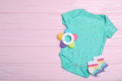 Photo of Child's clothes and teether on pink wooden background, flat lay. Space for text