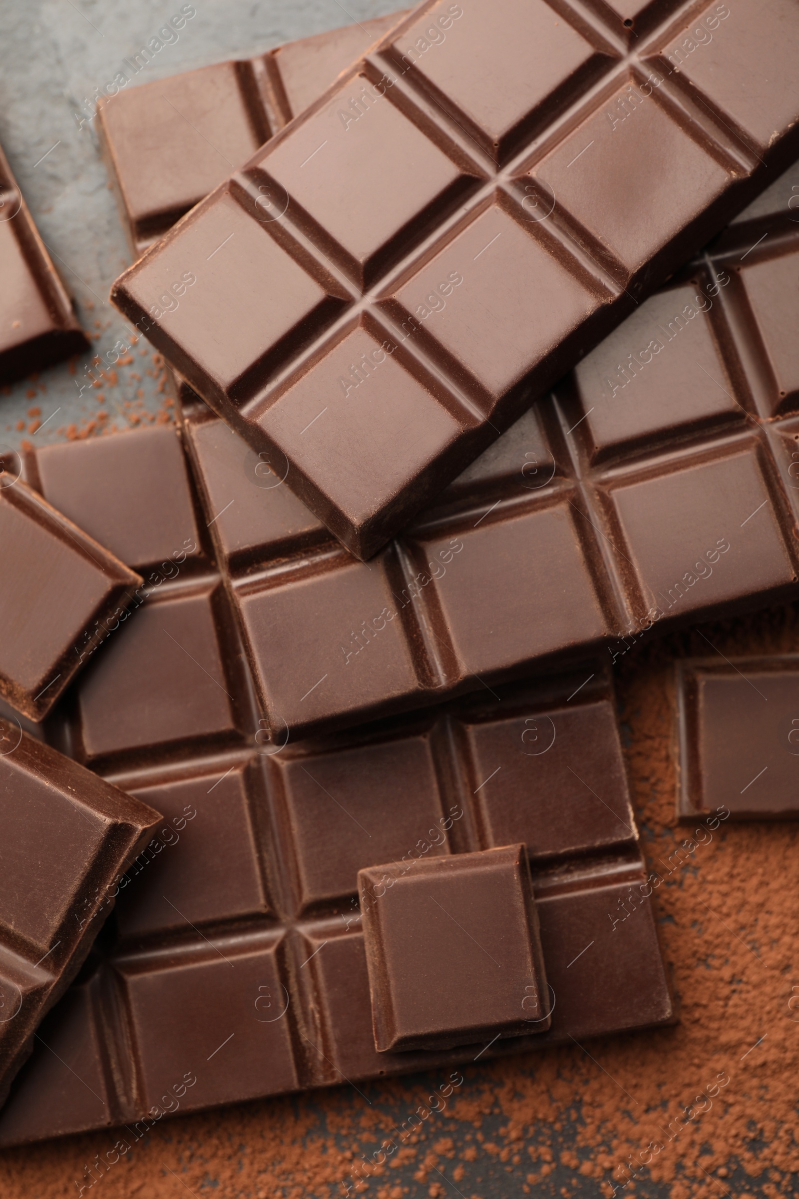 Photo of Delicious dark chocolate and cocoa powder on black table, flat lay