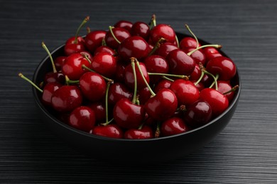 Photo of Bowl with ripe sweet cherries on dark wooden table, closeup