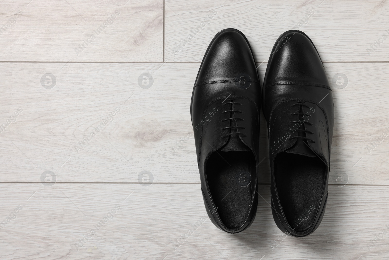 Photo of Pair of black leather men shoes on light wooden floor, top view. Space for text