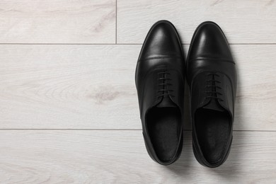 Pair of black leather men shoes on light wooden floor, top view. Space for text