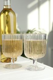 Alcohol drink in glasses and bottle on white wooden table indoors, closeup