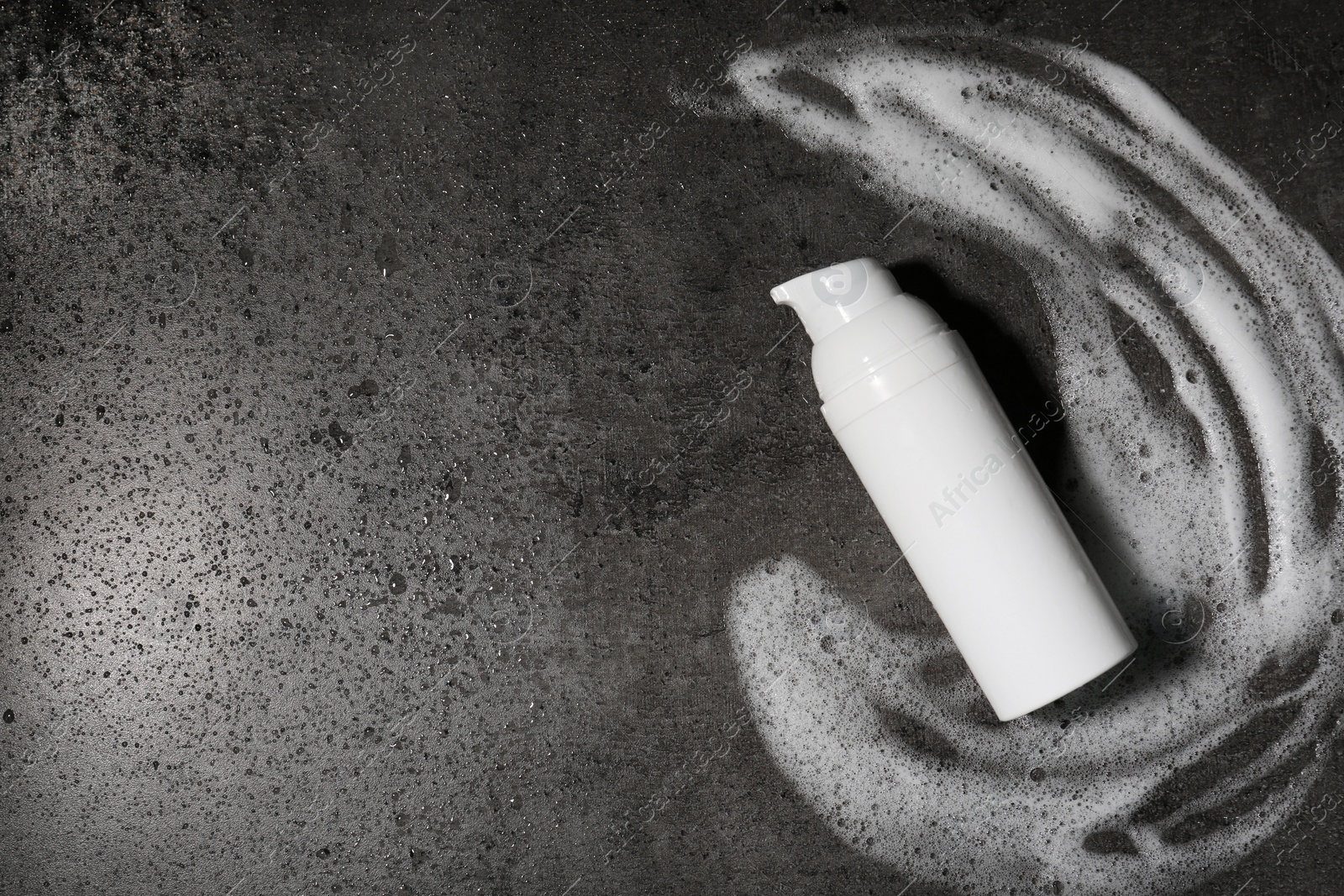 Photo of Bottle with cleansing foam on wet grey background, top view and space for text. Cosmetic product