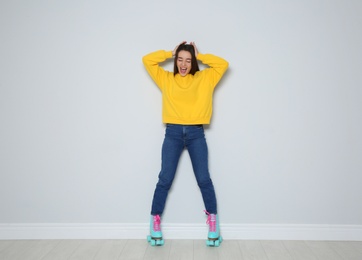 Full length portrait of young woman with roller skates near color wall