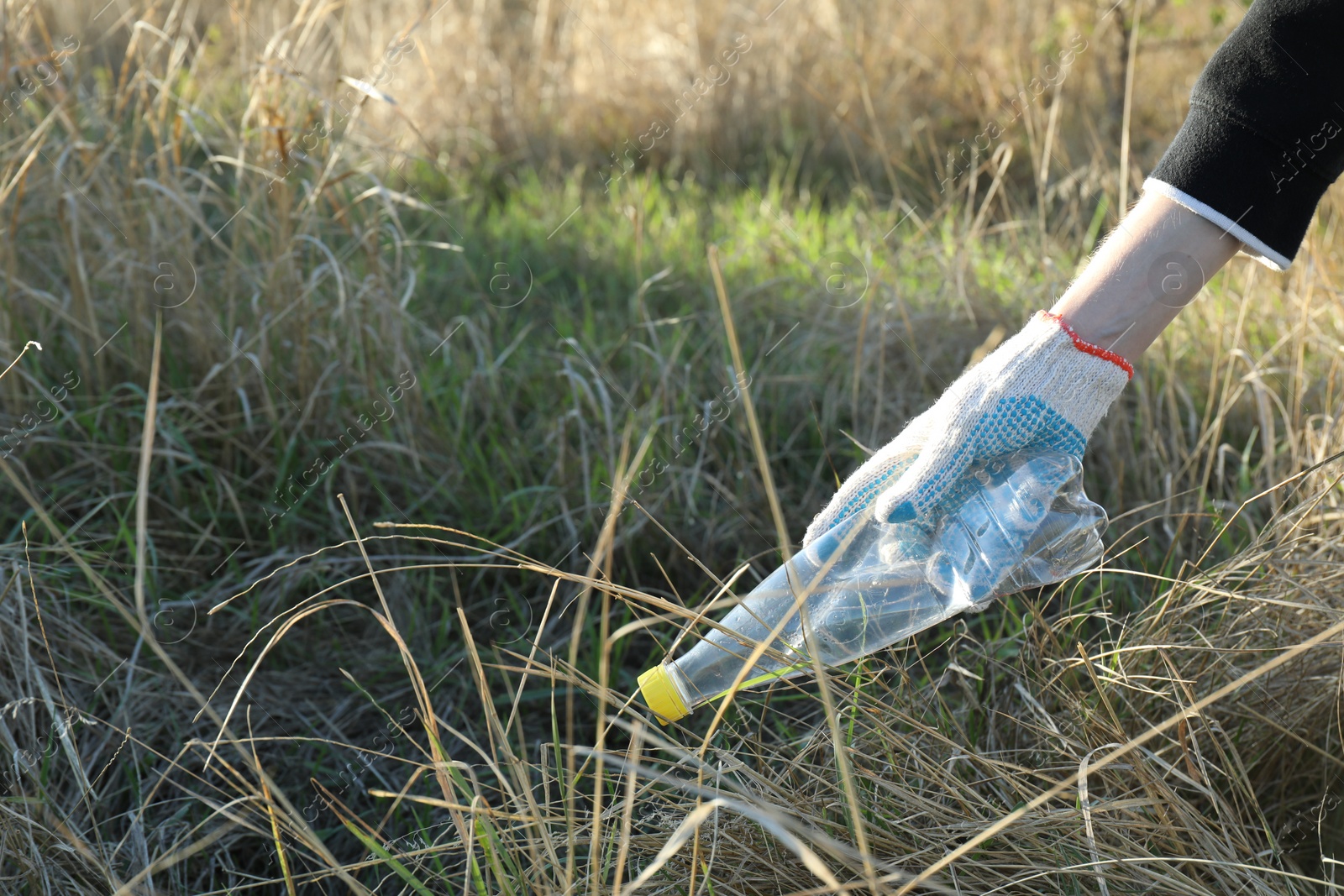 Photo of Woman picking up plastic bottle outdoors, closeup. Space for text