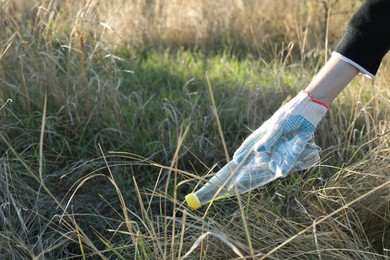 Photo of Woman picking up plastic bottle outdoors, closeup. Space for text