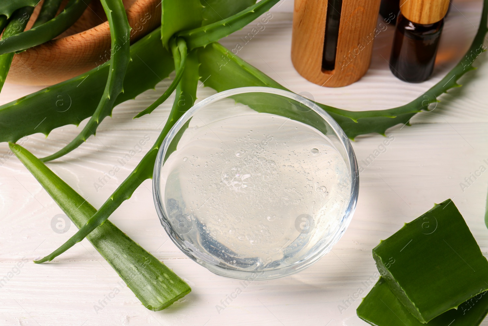 Photo of Bowl of cosmetic gel and cut aloe vera leaves on white wooden table, above view