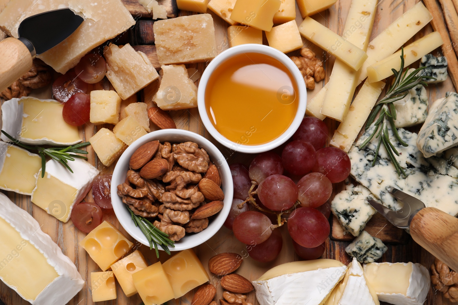 Photo of Cheese plate with honey, grapes and nuts on wooden board, top view