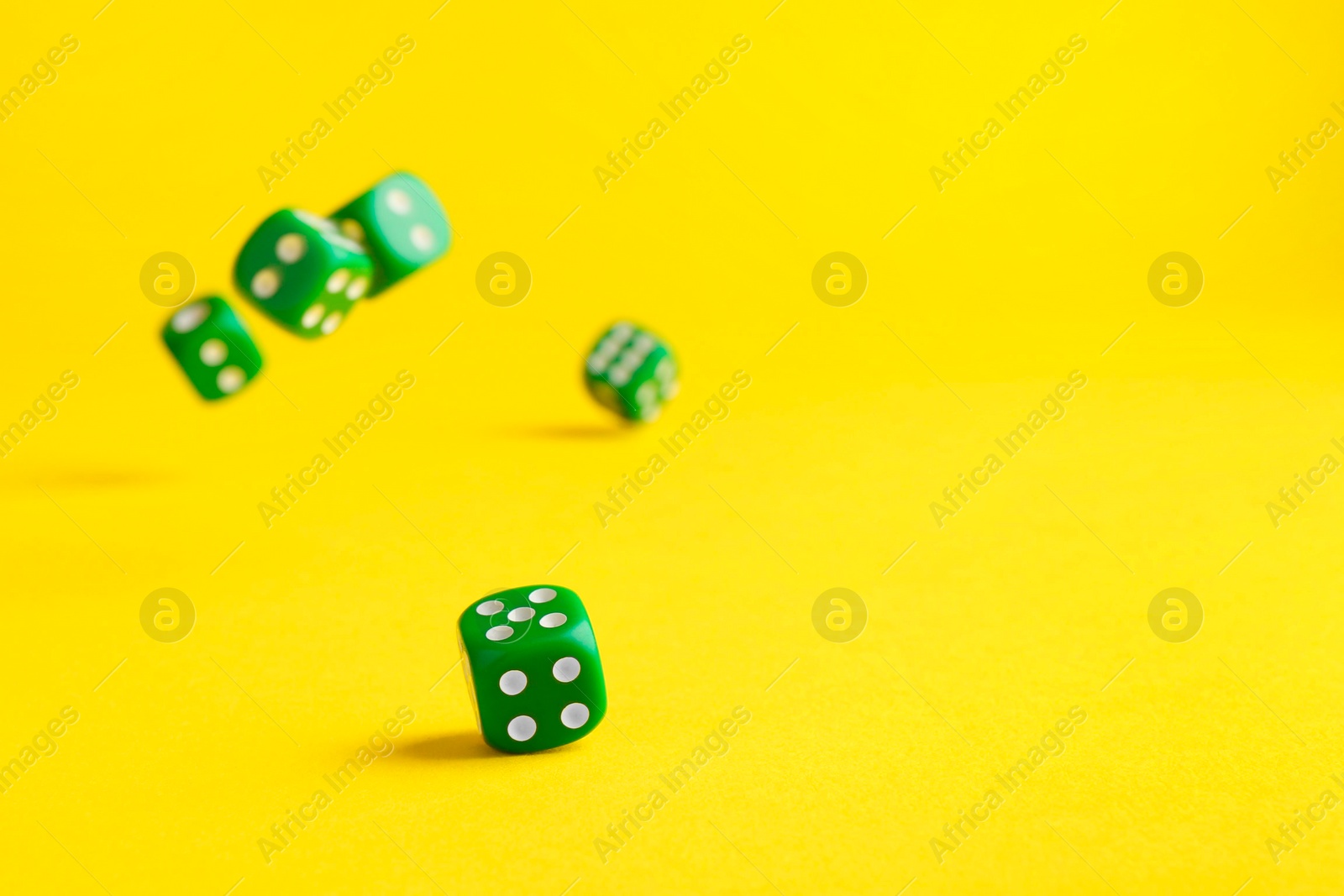 Photo of Many green game dices falling on yellow background. Space for text
