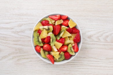 Delicious fresh fruit salad in bowl on white wooden table, top view