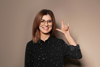 Photo of Woman showing I LOVE YOU gesture in sign language on color background