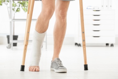 Photo of Man with broken leg in cast standing on crutches, indoors