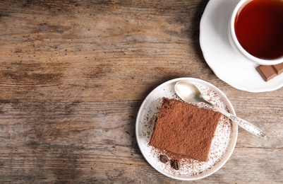 Photo of Flat lay composition with tiramisu cake and tea on wooden table, space for text