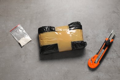 Photo of Packages with narcotics and stationery knife on grey textured table, flat lay