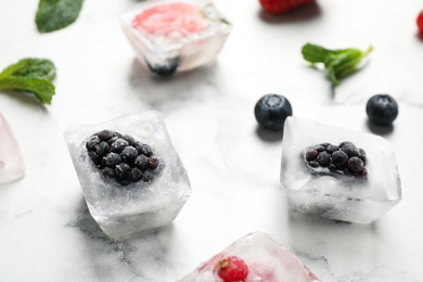 Photo of Ice cubes with blackberries on white marble table, closeup