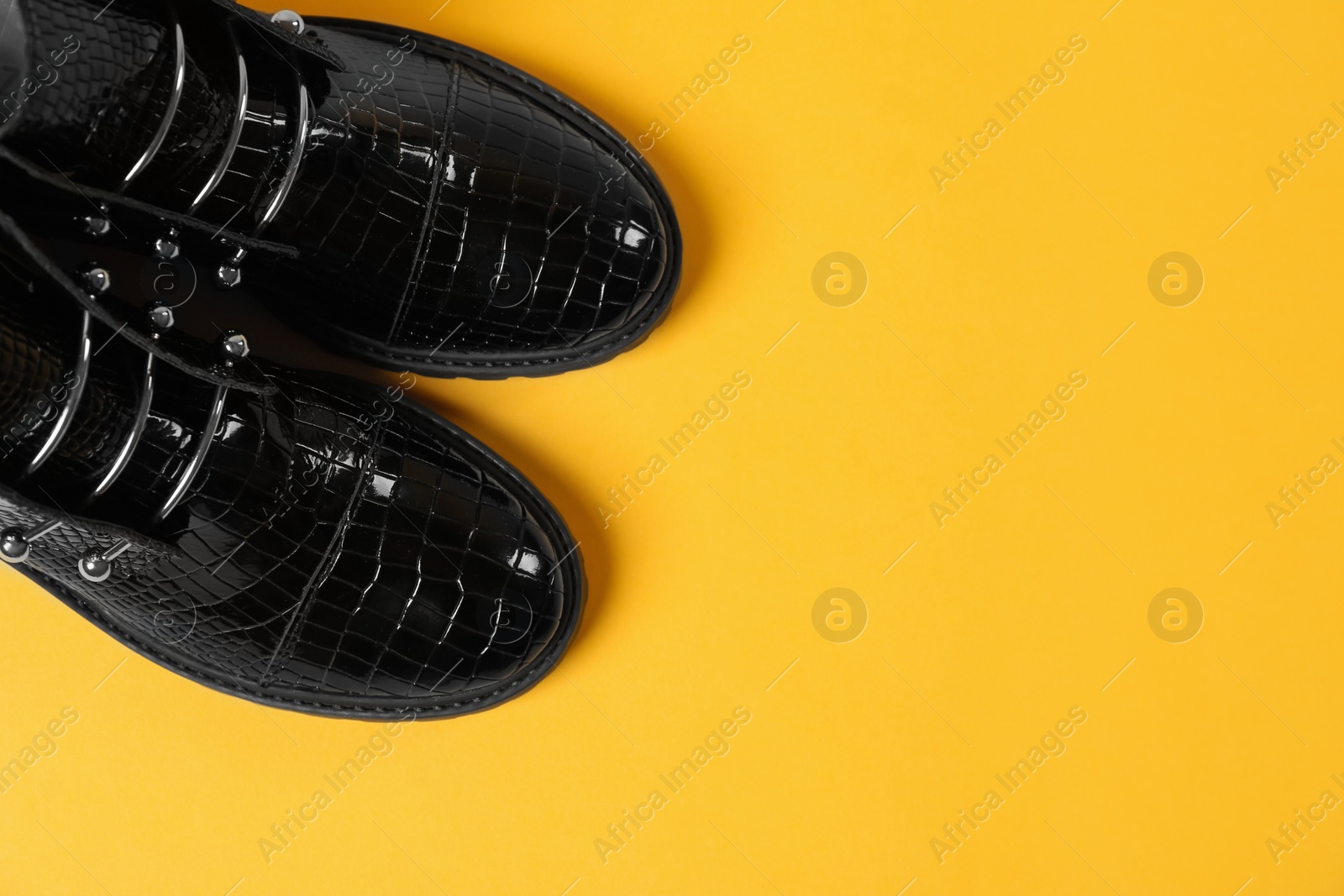 Photo of Pair of stylish ankle boots on yellow background, top view. Space for text