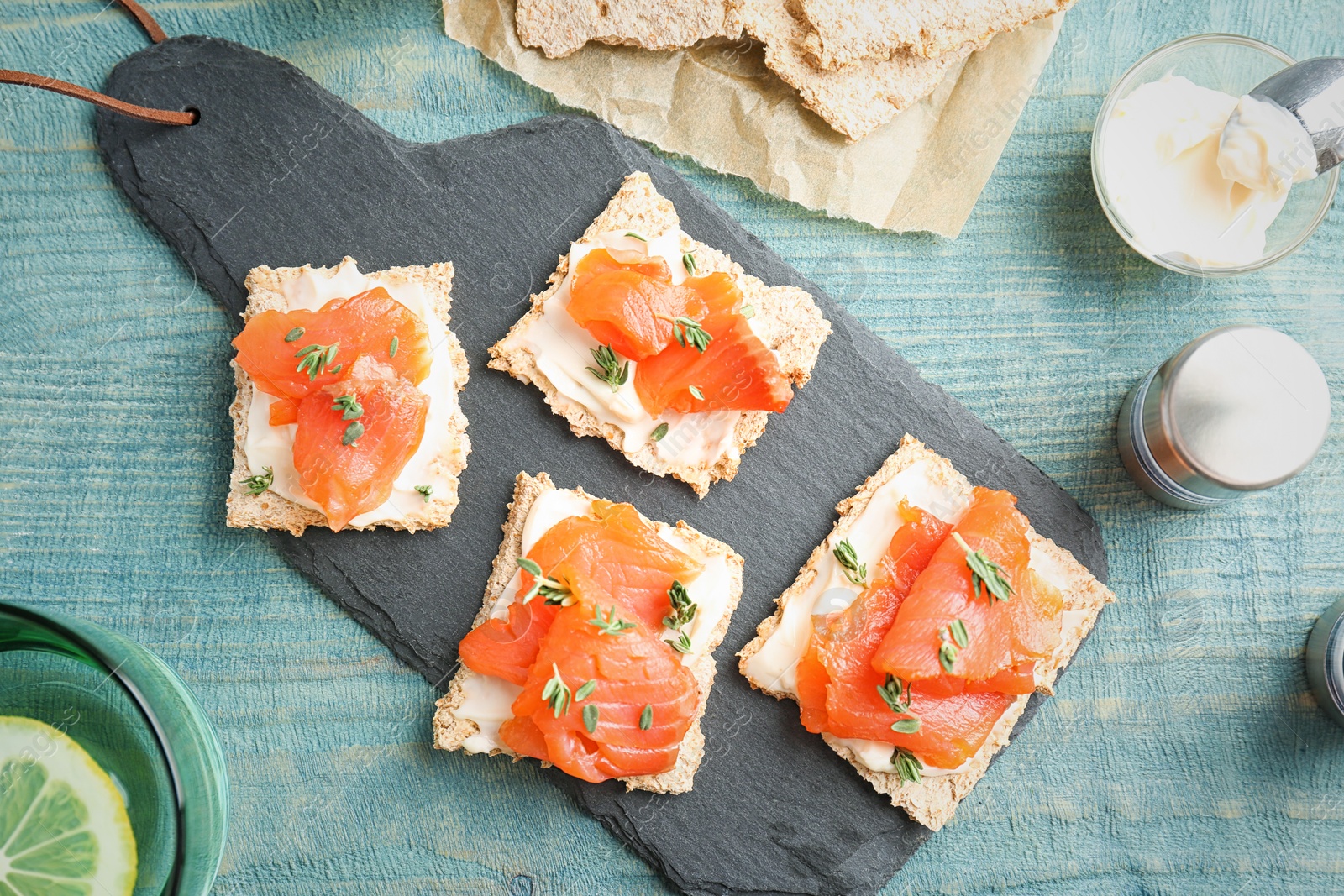 Photo of Crispbreads with fresh sliced salmon fillet on slate board, top view