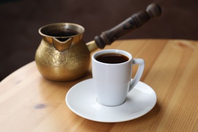 Photo of Turkish coffee. Freshly brewed beverage in cup and cezve on wooden table