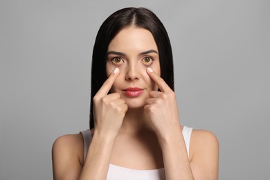 Woman checking her health condition on grey background. Yellow eyes as symptom of problems with liver