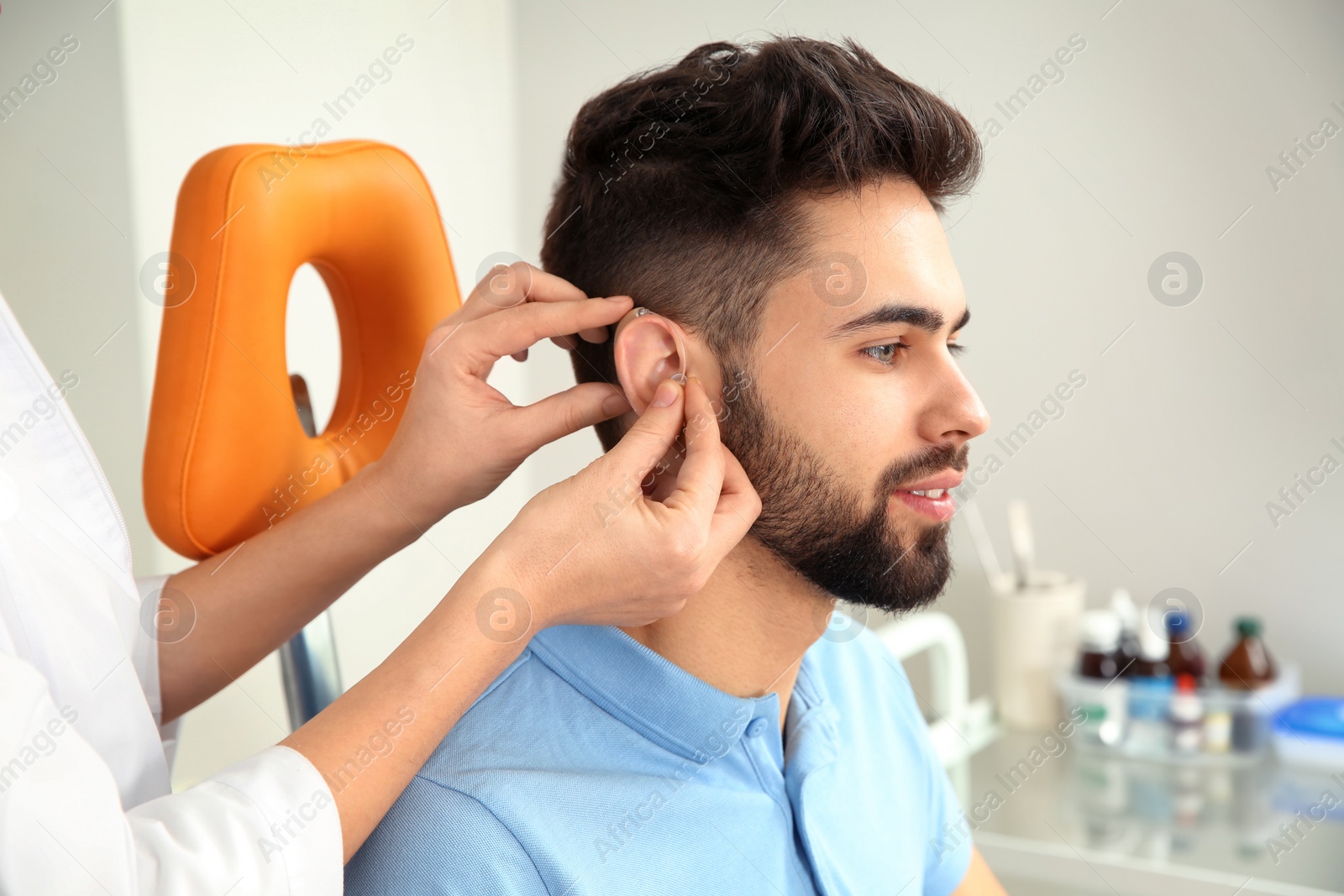 Photo of Otolaryngologist putting hearing aid in patient's ear at clinic