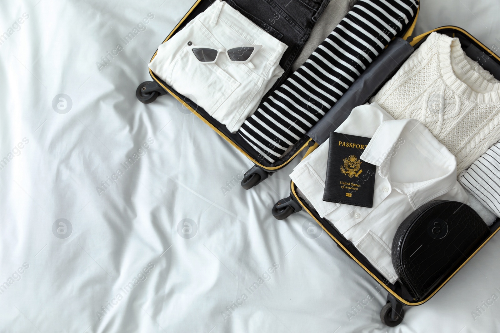 Photo of Open suitcase with clothes, passport and accessories on bed, top view. Space for text