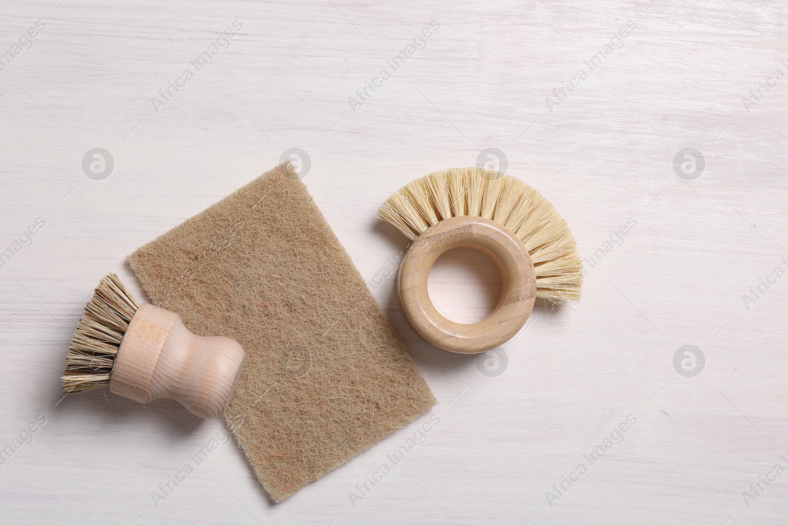 Photo of Cleaning brushes and sponge on light wooden table, top view