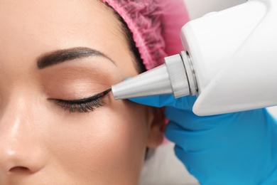 Photo of Woman undergoing laser tattoo removal procedure in salon, closeup