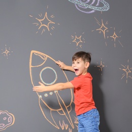 Cute little child playing with chalk rocket drawing on grey background